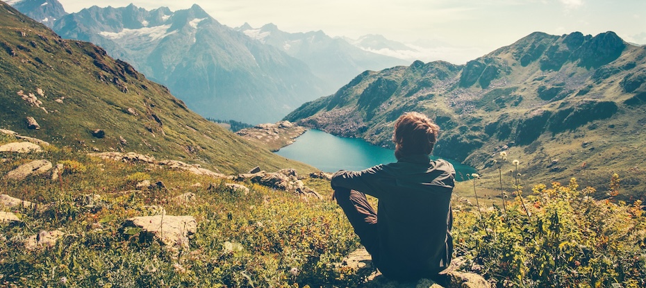 Man sitting by mountain lake, connecting with nature for inner peace and well-being